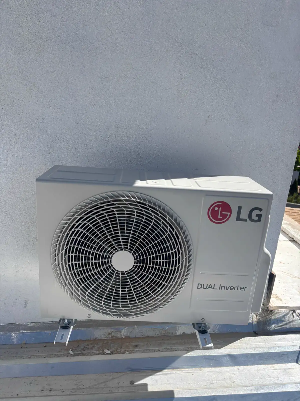 Condensadora LG Dual Inverter recém-instalada sobre suportes, vista de frente, com a grade do ventilador em destaque.